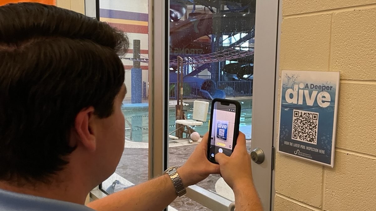 Person uses smartphone to scan a QR code outside a public pool.