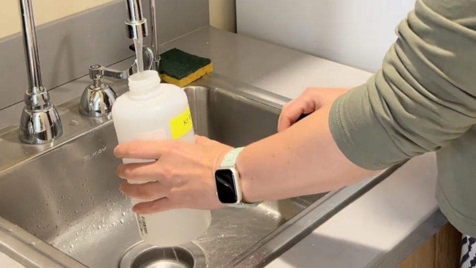 Professional holds a bottle under running water from a faucet to collect a water sample.