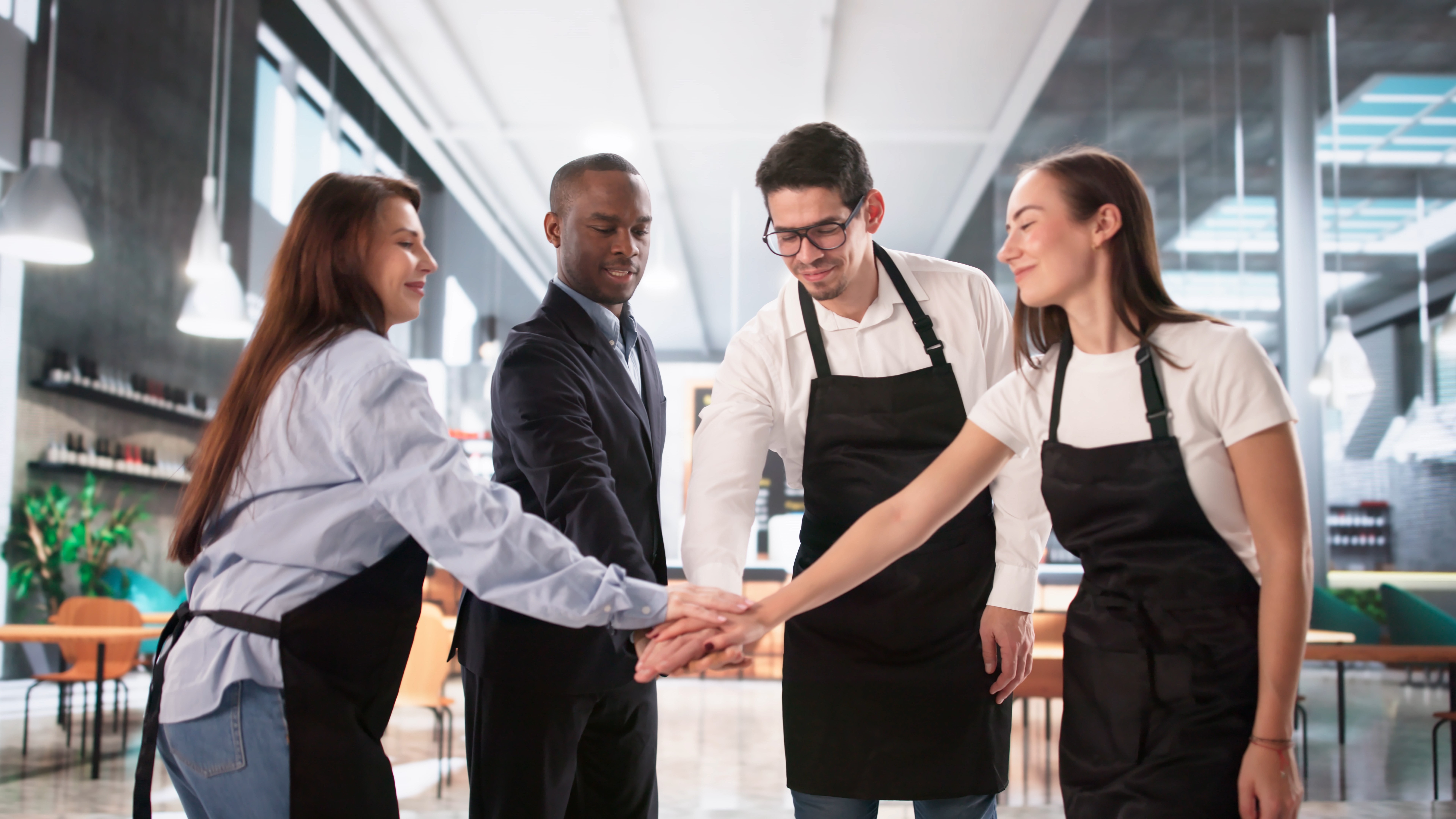 Food workers and a person in a business suit join hands in a restaurant kitchen