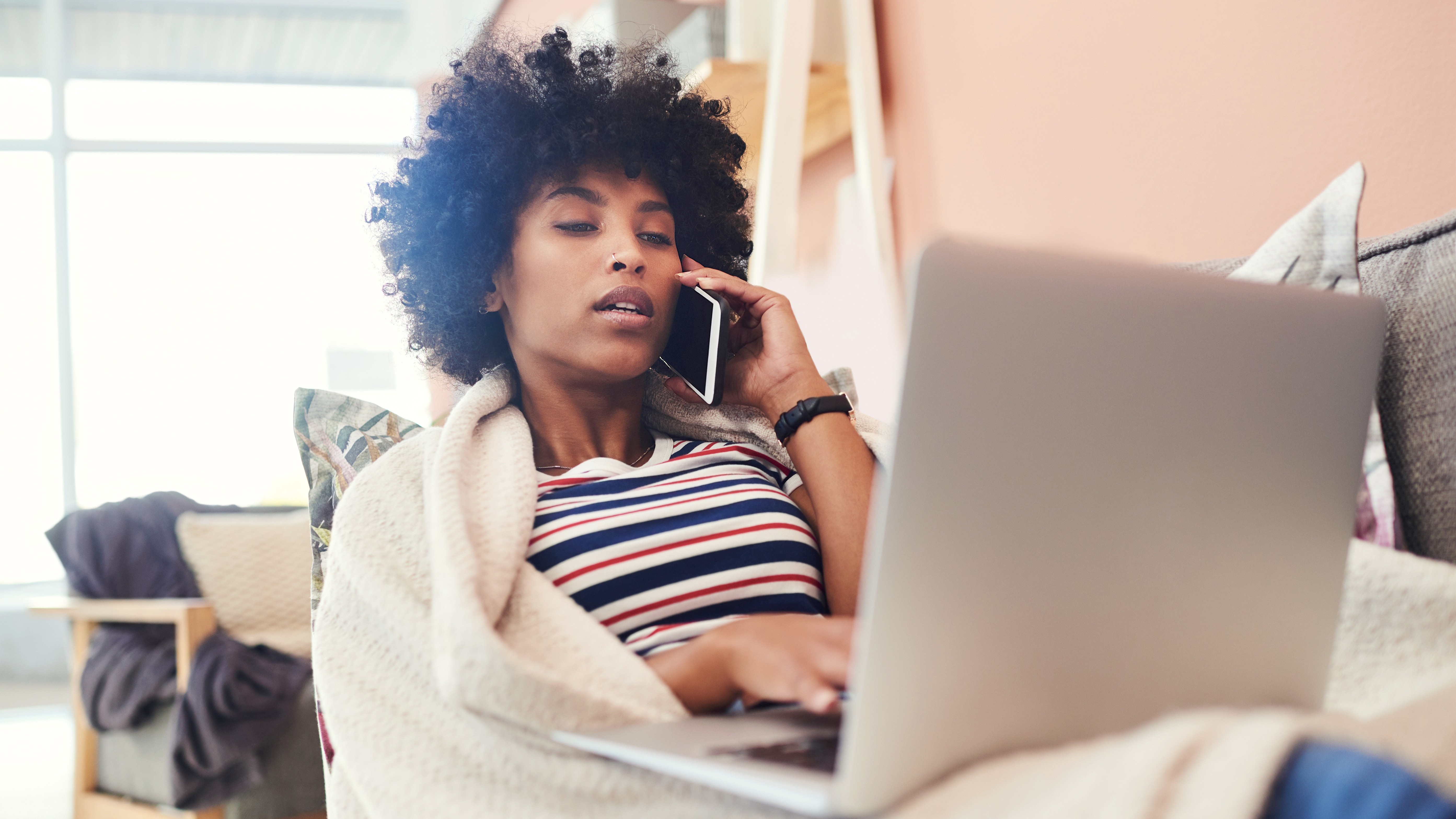 Woman not feeling well on a couch using her laptop and phone