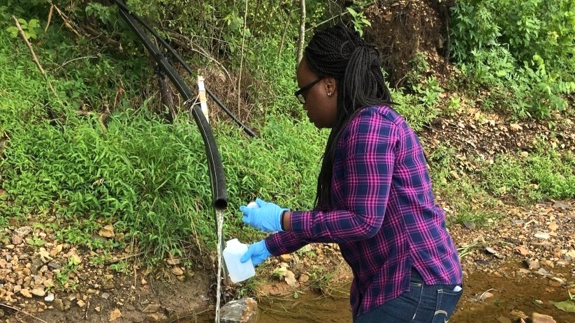 Environmental health intern taking a water sample outside.