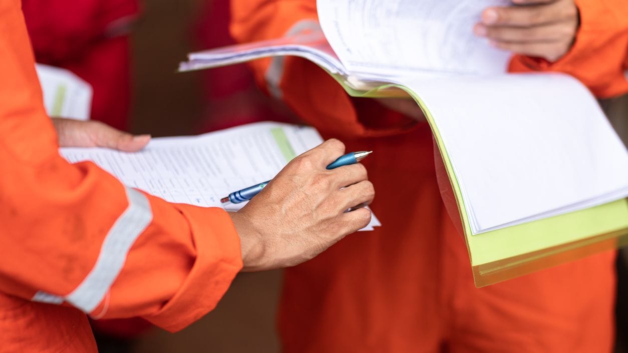 People in orange safety suits looking at documents and clipboards