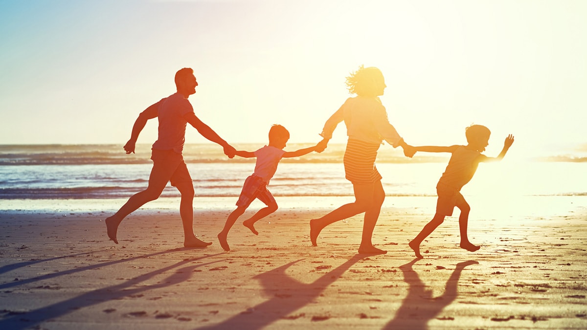 Family of four running on beach at sunset