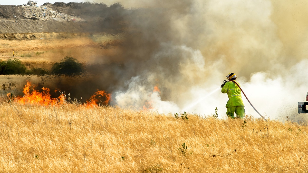 Firefighter using hose to combat wildland fire in prairie grass
