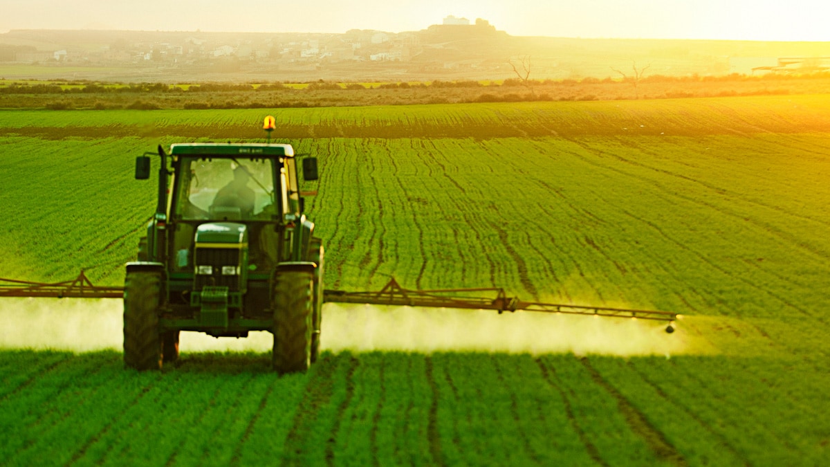 Green tractor spraying pesticides on agricultural crops.