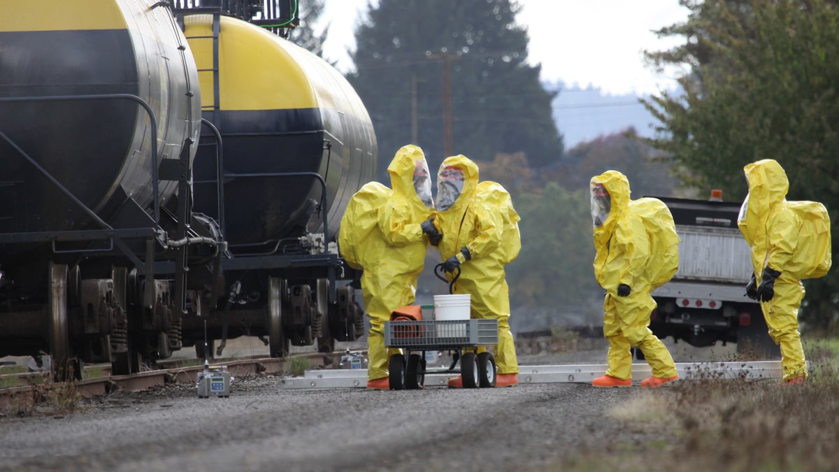 People investigating toxic substances near train while wearing hazmat suits.