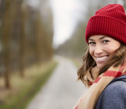 Woman wearing a red hat and plaid scarf is smiling and walking outdoors.