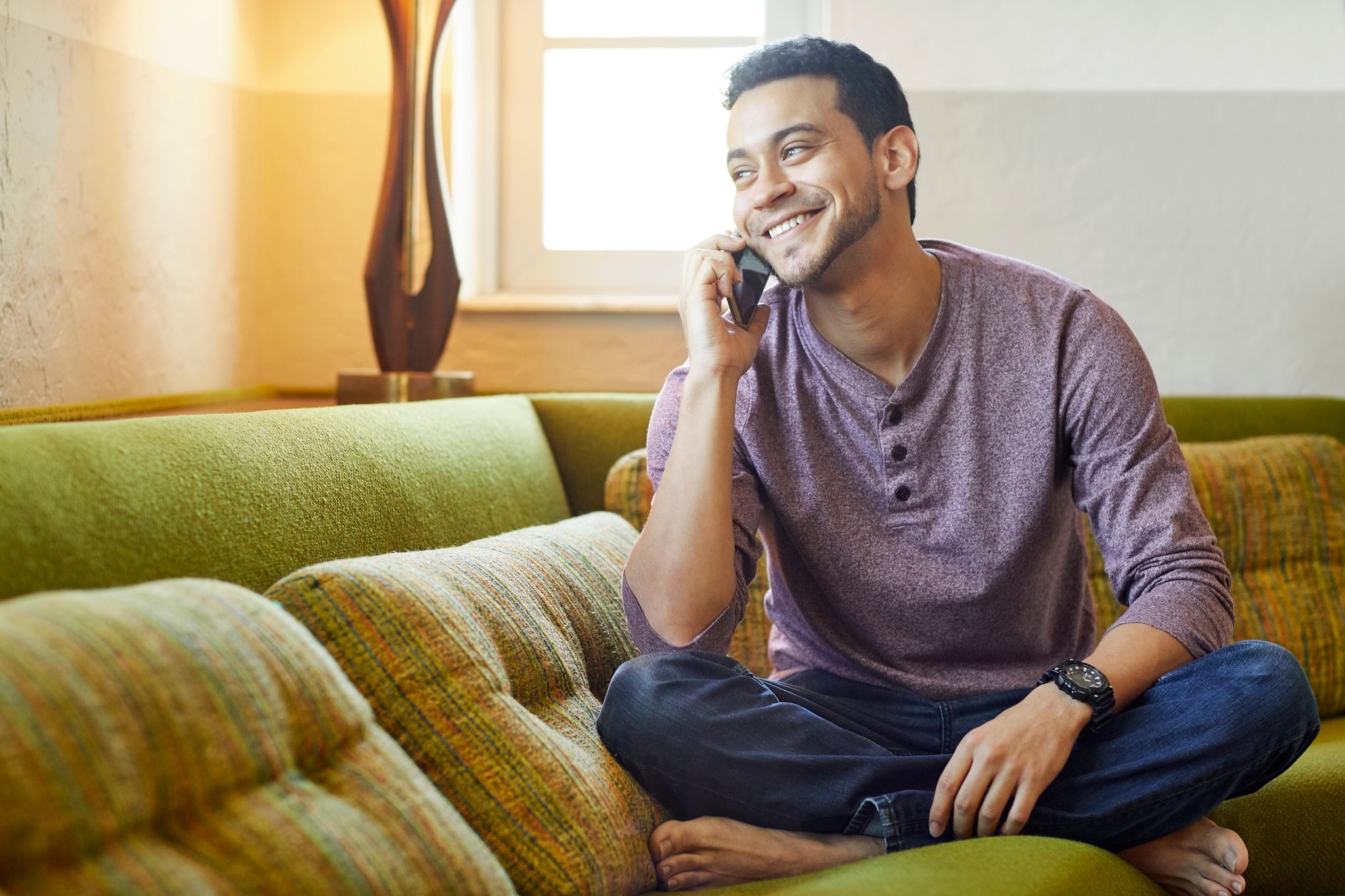 Smiling young man talking on the phone while sitting on the couch.