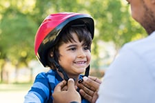 A young boy is smiling as his father is putting his helmet on him.