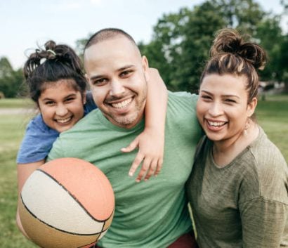 A mom, dad, and young girl are hugging and playing basketball.