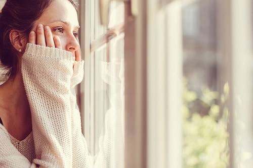 A sad young woman stares out a window.
