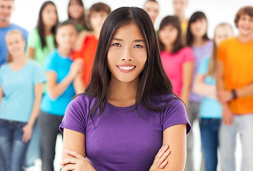 Young woman wearing a purple shirt standing with a large group of people behind her.