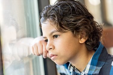 Young boy rests his head on his hand and stares out a window.