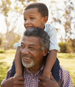 Older black man carries small boy on shoulders in the park