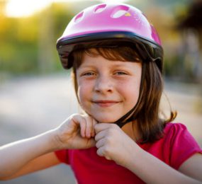 Young girl putting on bicycle helmet and smiling.