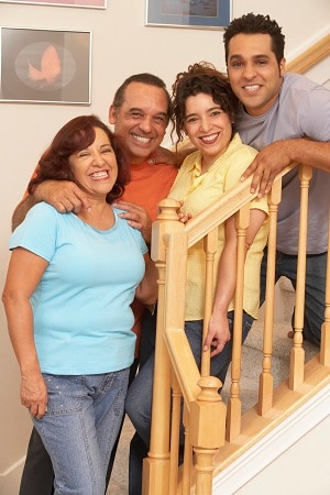 una famila de cuatro personas, sonrientes, parados en la escalera de su casa