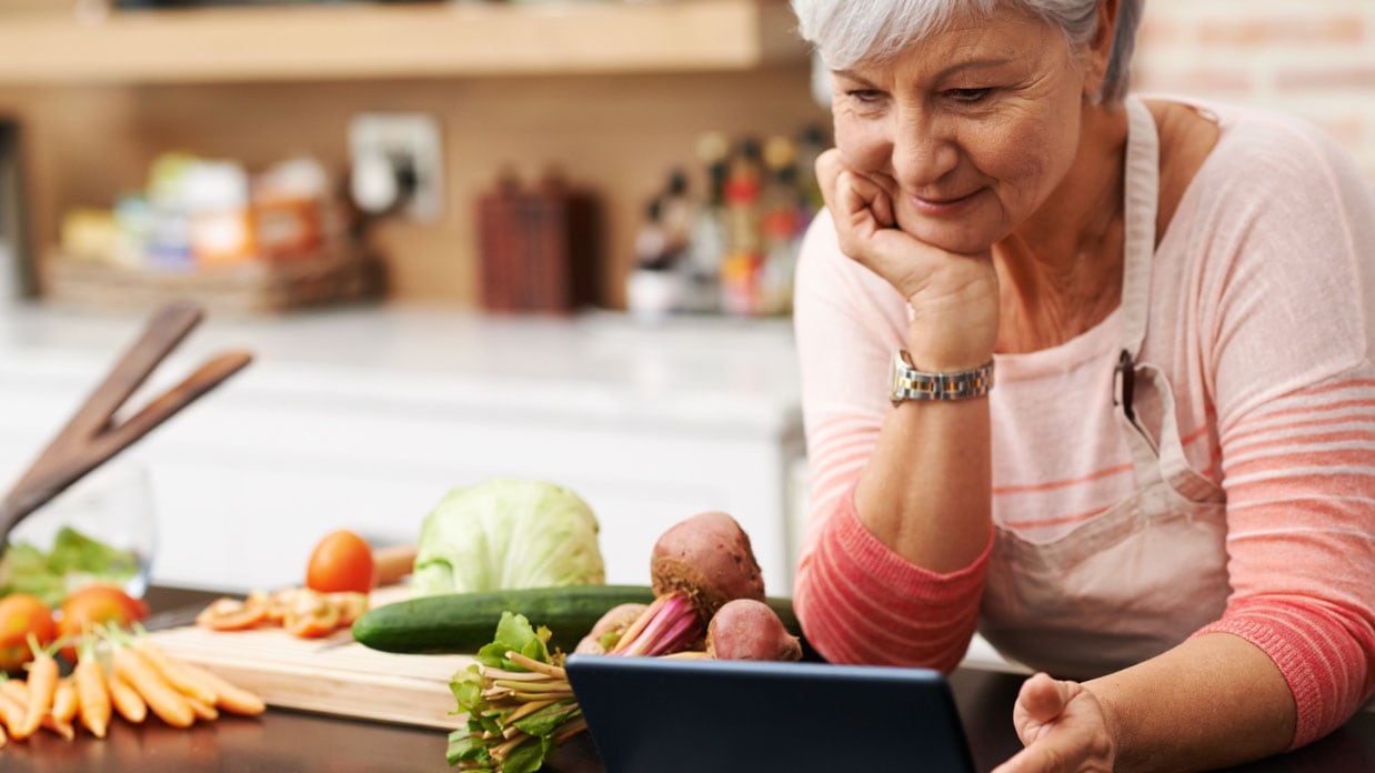Senior woman reading recipe on tablet while preparing vegetables.