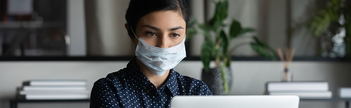 Woman wearing a mask while she works on the computer in an office setting.