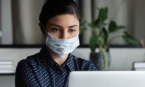Una mujer con una máscara mientras trabaja en la computadora en un entorno de oficina.