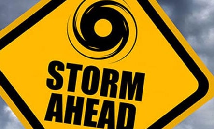 Una señal de precaución amarilla en una carretera que dice TORMENTA ADELANTE y tiene un ícono de huracán.