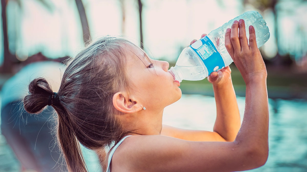 Young girl is drinking from a water bottle on a hot day