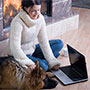 Woman sitting on floor with dog and laptop in front of fireplace