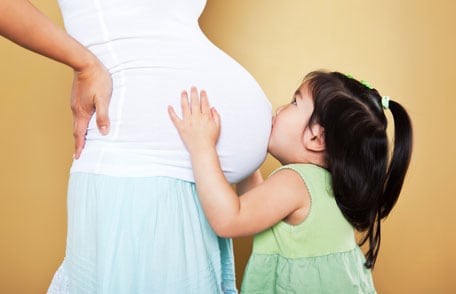 Little girl kissing pregnant mother's belly