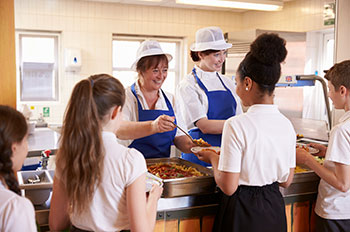 Photo of two women serving kids food in a school cafeteria