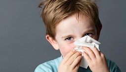 A young boy using a tissue to clean his nose.