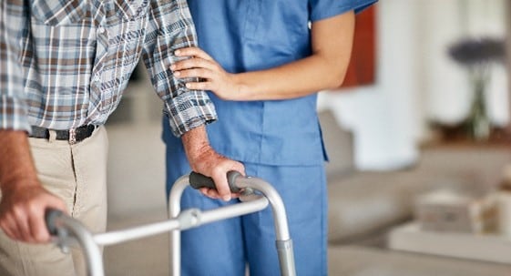 Miembro del personal de atención médica ayudando a alguien a usar un andador