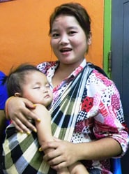 In Laos, a young mother and holds her baby and receives information about seasonal flu.