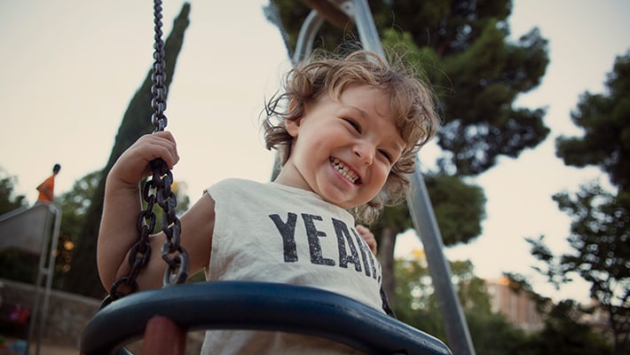 Child smiling while swinging outside.