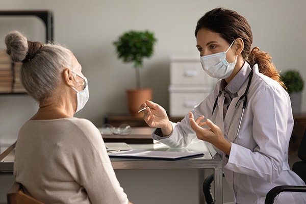 A female doctor talking with elder patient and both wearing masks.