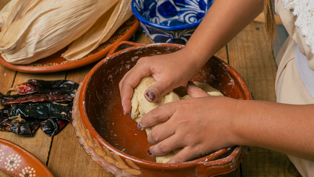 A person working corn masa dough to make tortillas on a wooden table.