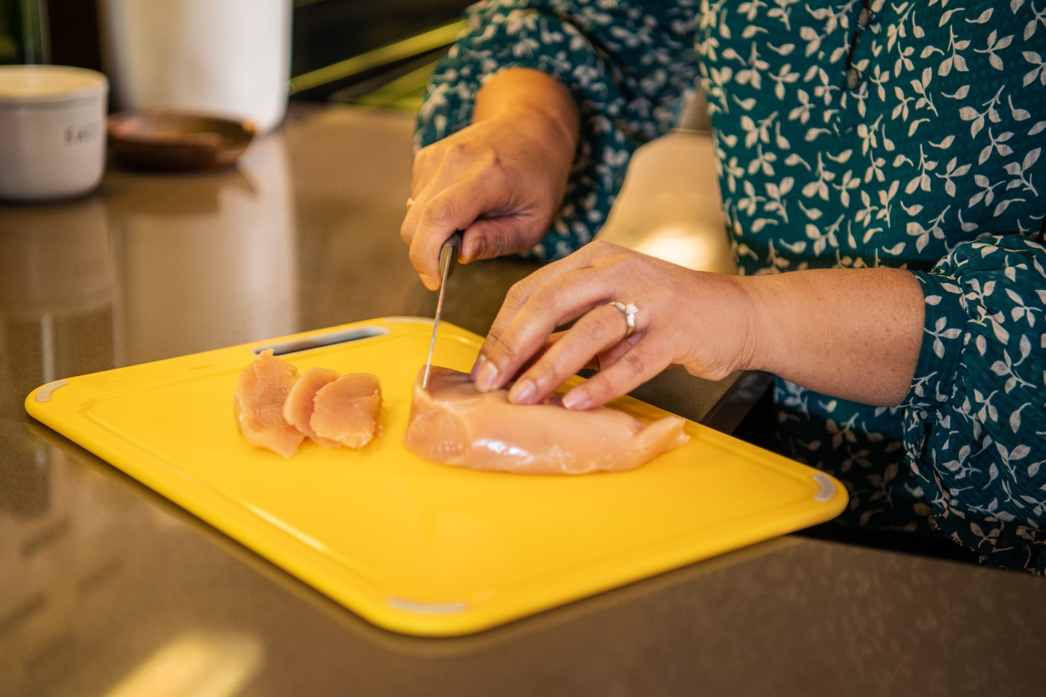 Woman cutting raw chicken on a clean, plastic cutting board.