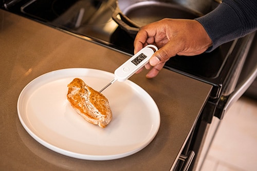 Man sticking a meat thermometer into a piece of cooked chicken.