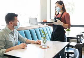 Man wearing a mask being served by a waitress wearing a mask.