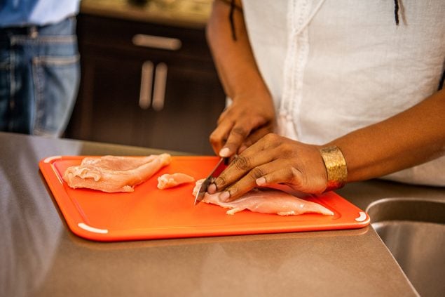 Person cutting chicken on a cutting board.