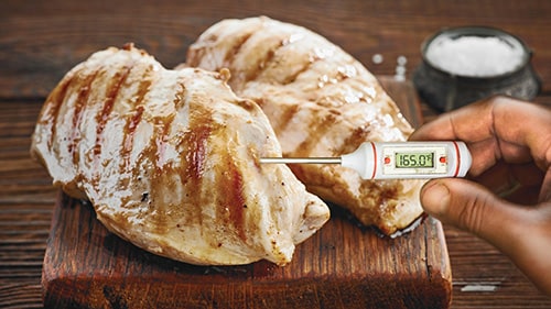 Person inserting a food thermometer into a piece of grilled chicken