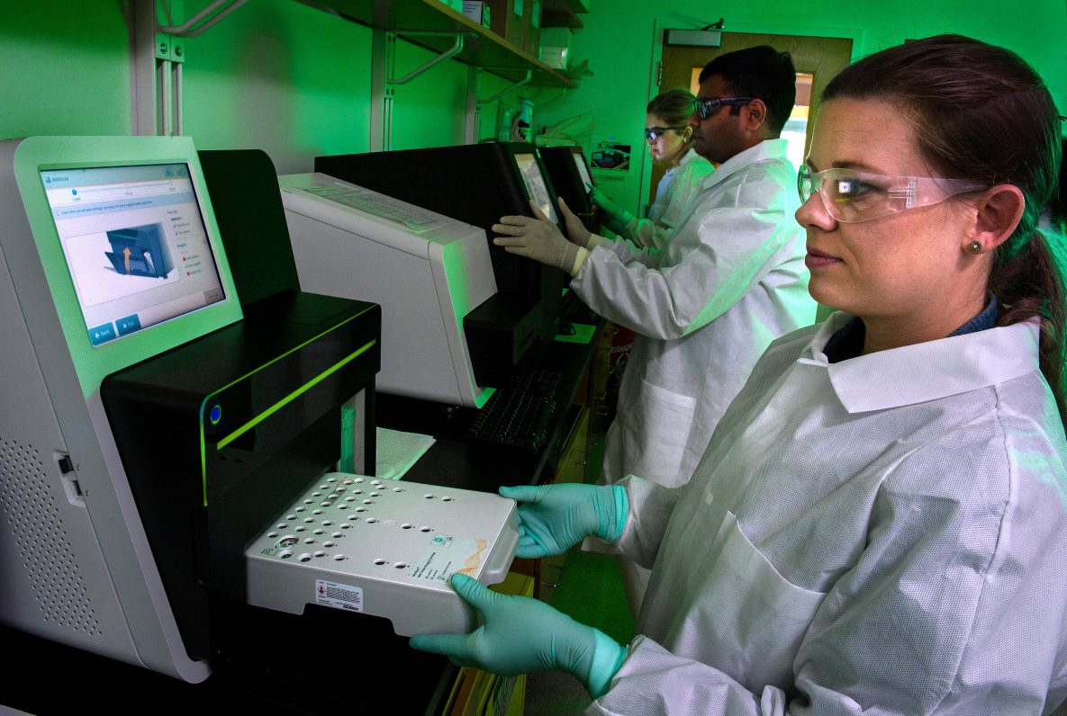Lab technician inserting samples into machine for analysis.