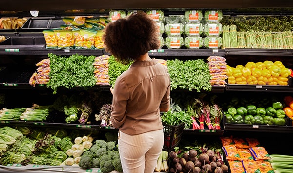 Person looking at vegetables on shelves in a grocery store.
