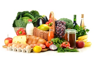 Picture of assorted fruits, vegetables, bread, beverages, cheese, and eggs arranged in baskets and on a table