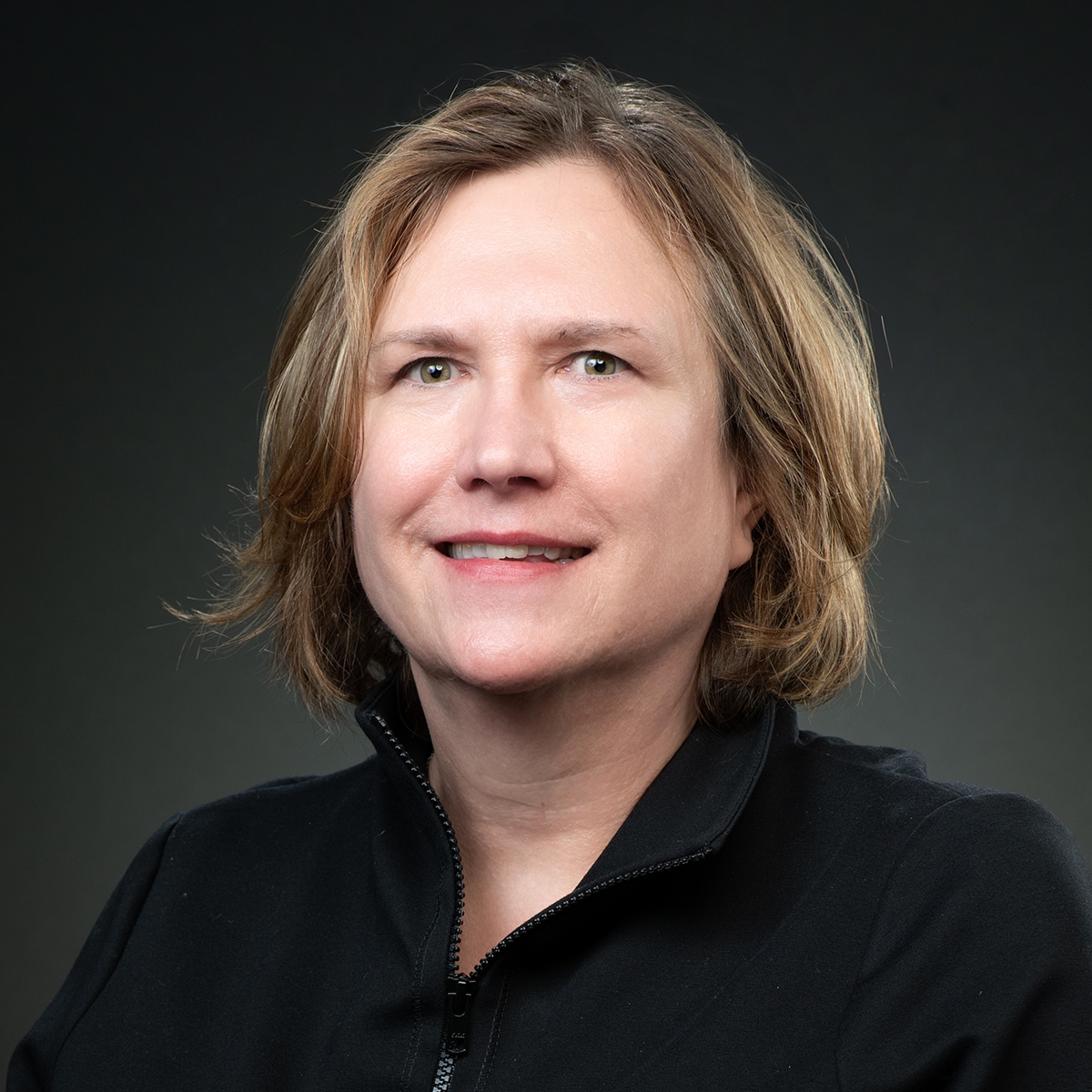 Kristin Pope is the Deputy Director of Management, Operations, Policy and Communications for the Center for Forecasting and Outbreak Analytics. She has short blond hair, against a dark grey background, wearing a black shirt.