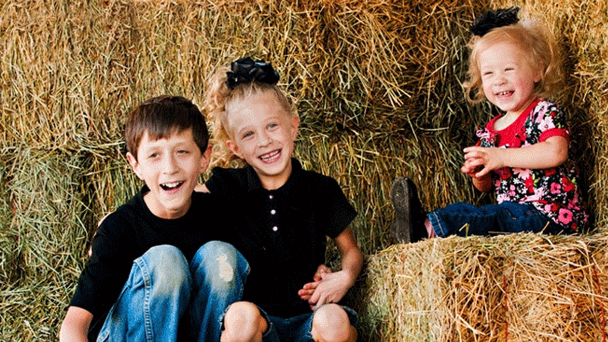 three kids with fxs sitting on haystack