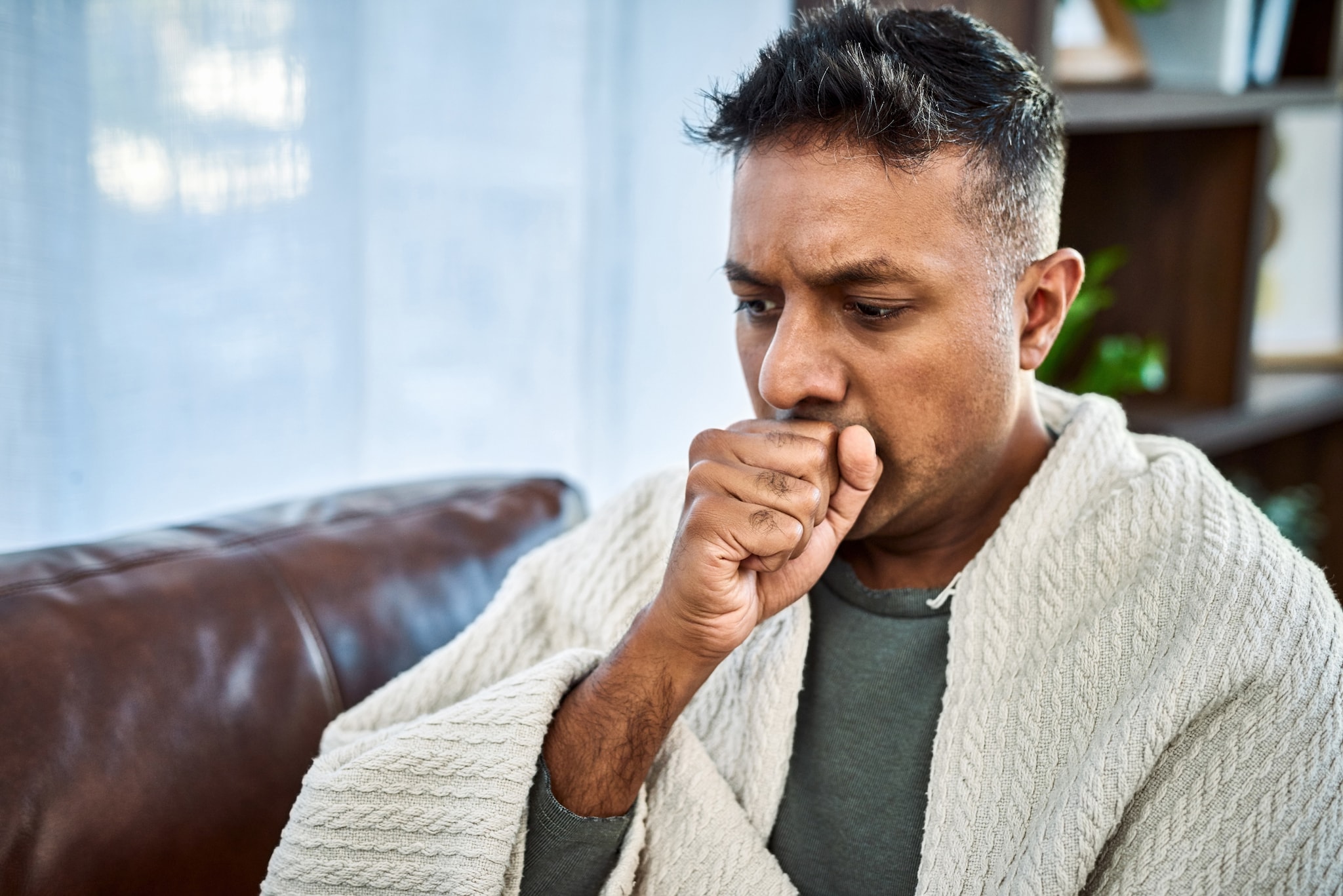 Stock image of a man coughing while covering his mouth with his fist.