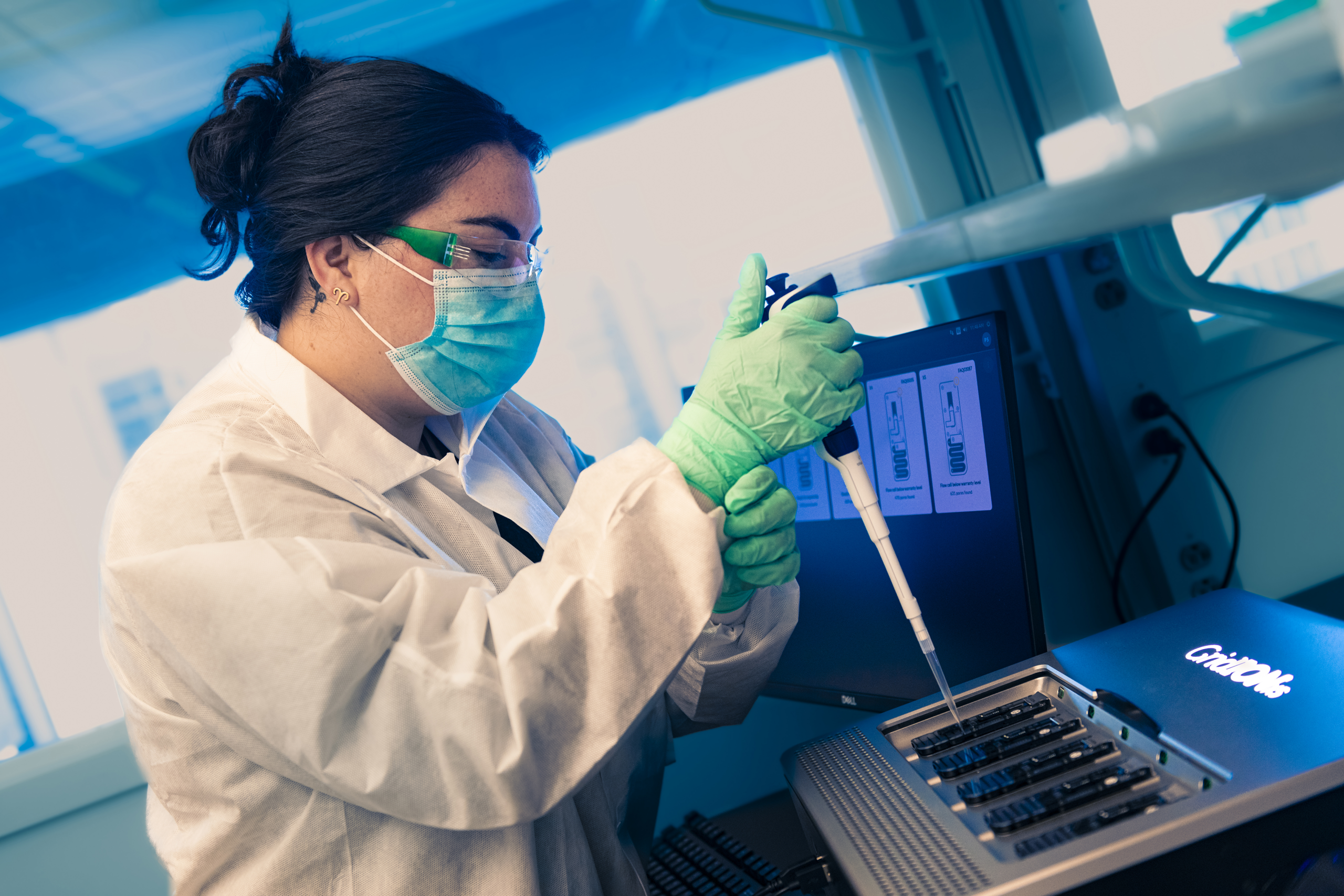 female lab worker wearing a gown, gloves, mask, and eye covering, preparing materials for sequencing