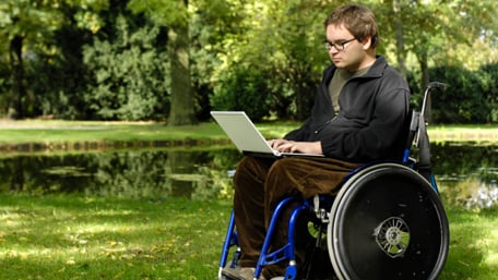 a person working on his laptop sittting in a wheelchair in a park