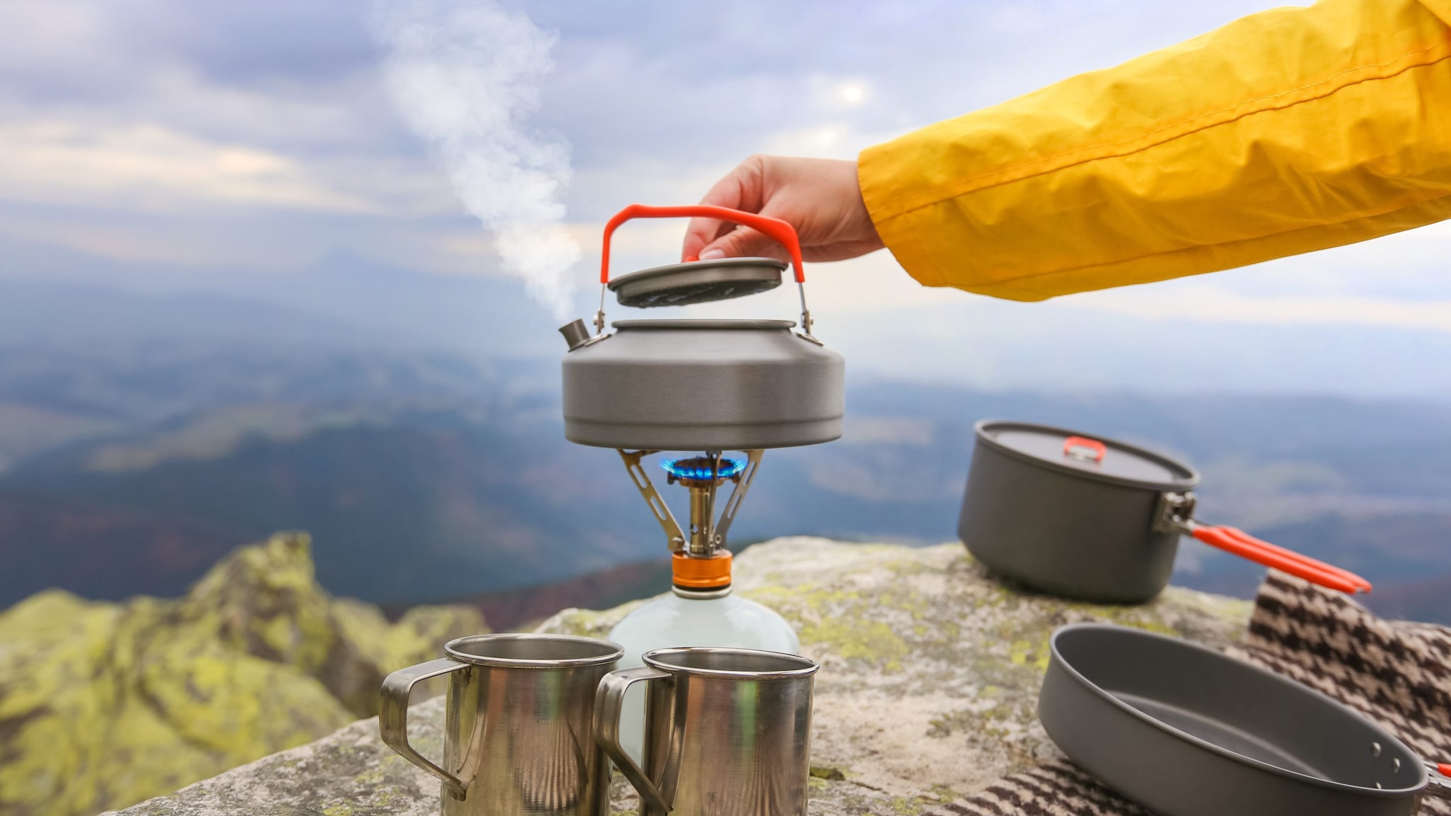 Hiker boiling water in a kettle with mountains in the background