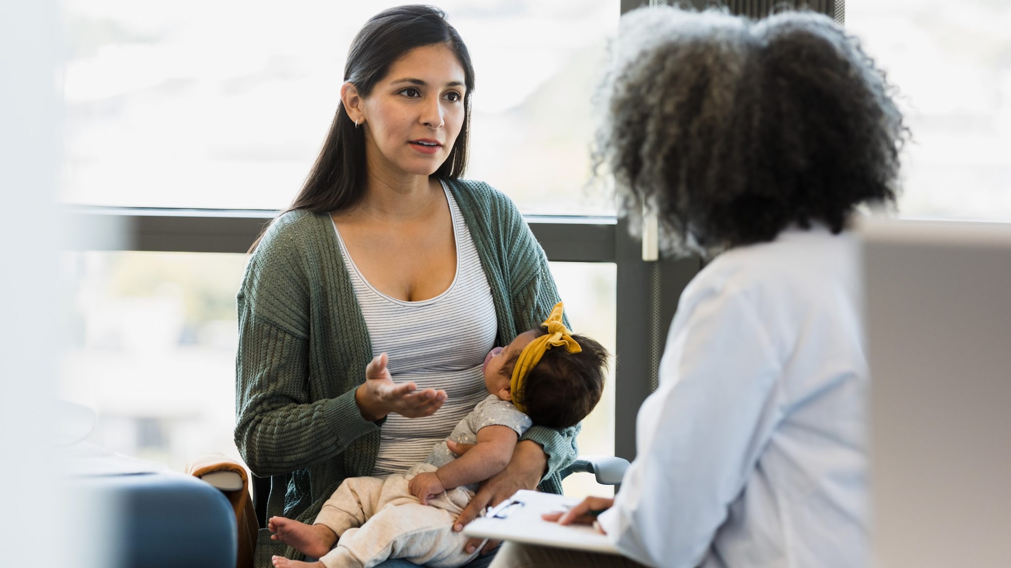 Woman holding a baby and talking to a healthcare provider in a doctor's office