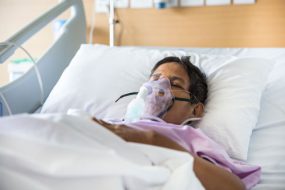 Adult in a hospital bed with an oxygen mask to help with breathing